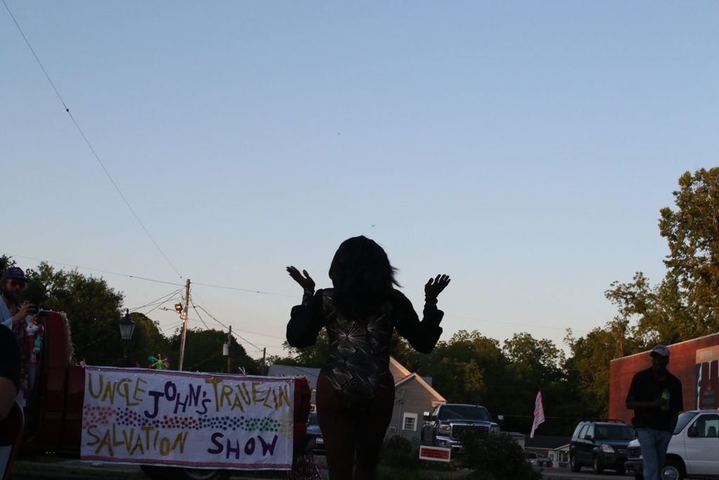 Drag performer in silhouette with sky and sign "Uncle John's Traveling Salvation Show."