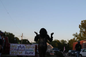 Drag performer in silhouette with sky and sign "Uncle John's Traveling Salvation Show."