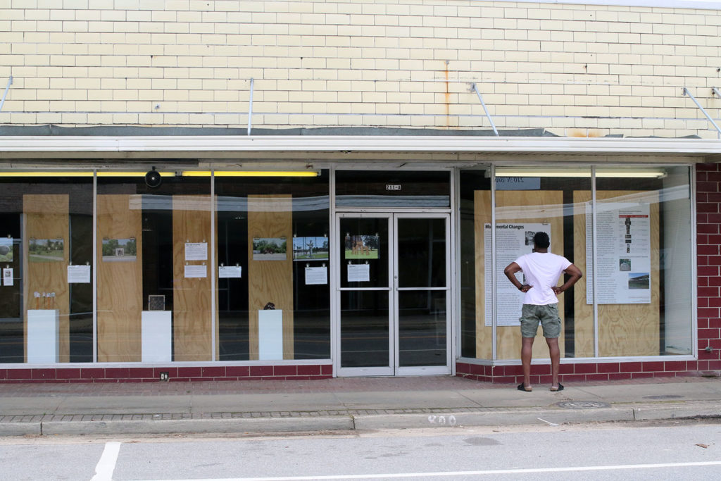 African American man stands wide legged, hands on hips reading text panel in store front window