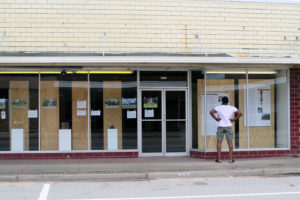 African American man stands wide legged, hands on hips reading text panel in store front window