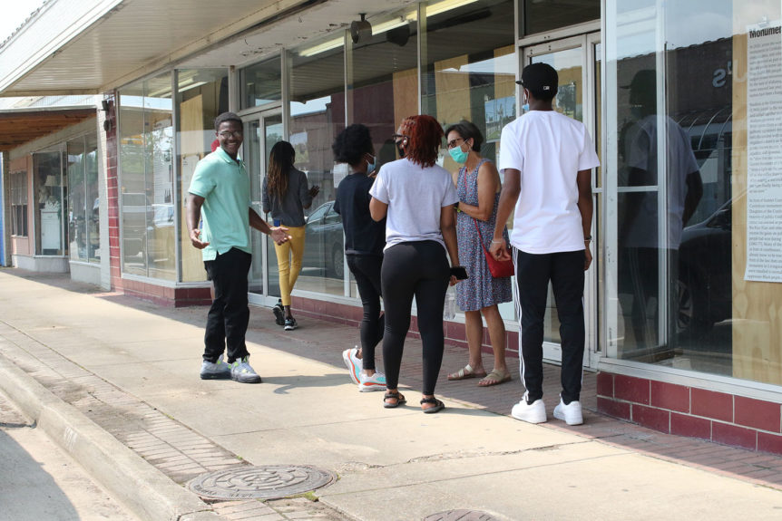 Color photograph of a young African American person in mint green shirt opens arms in a confident, welcoming manner.